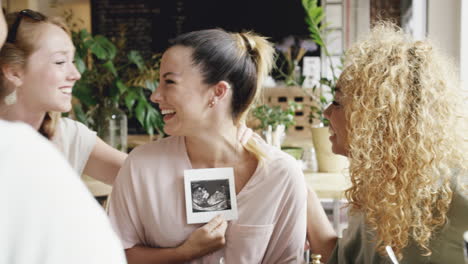 pregnant woman showing ultrasound picture of baby to friends celebrating