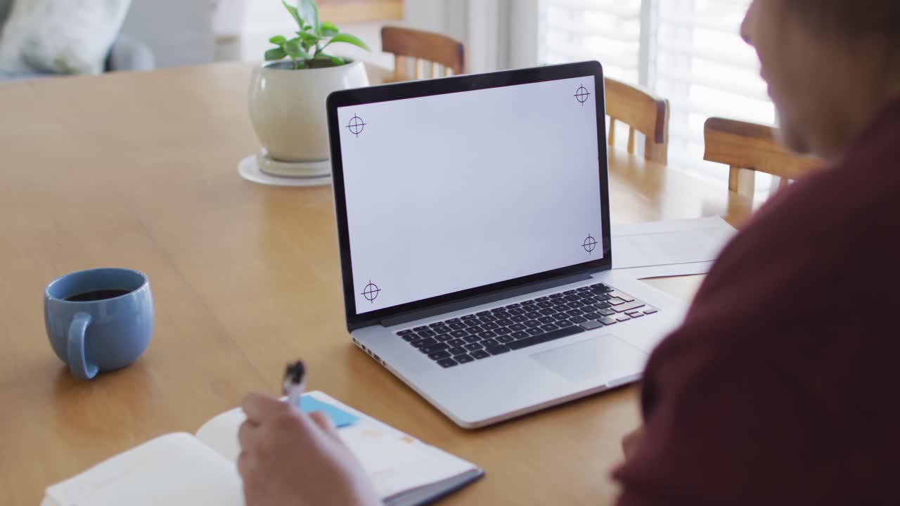 African american senior woman at dining table, using laptop with copy space on screen and writing