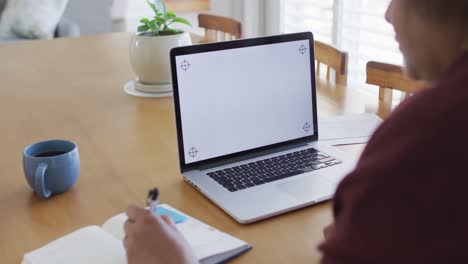 Mujer-Mayor-Afroamericana-En-La-Mesa-Del-Comedor,-Usando-Una-Computadora-Portátil-Con-Espacio-Para-Copiar-En-La-Pantalla-Y-Escribiendo