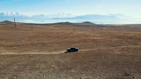 four-wheel drive truck driving along a dirt road with a lake and snowy mountains in the distance - aerial view