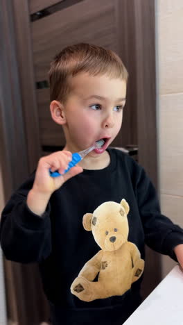 baby boy wearing a sweater with teddy brushing teeth. cheerful kid uses flashing tooth brush. hygiene and health. vertical video.