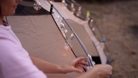 woman setting up string lights on a tent