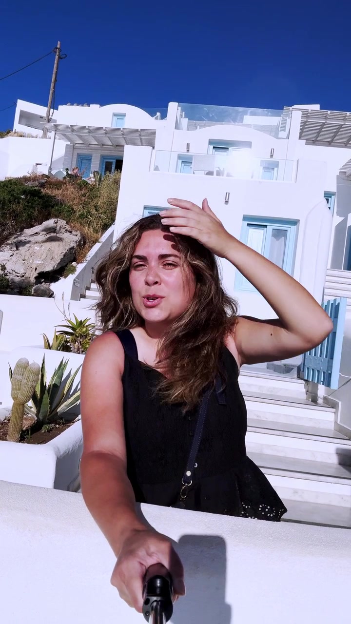 Woman waving hello in santorini greece holding a selfie stick