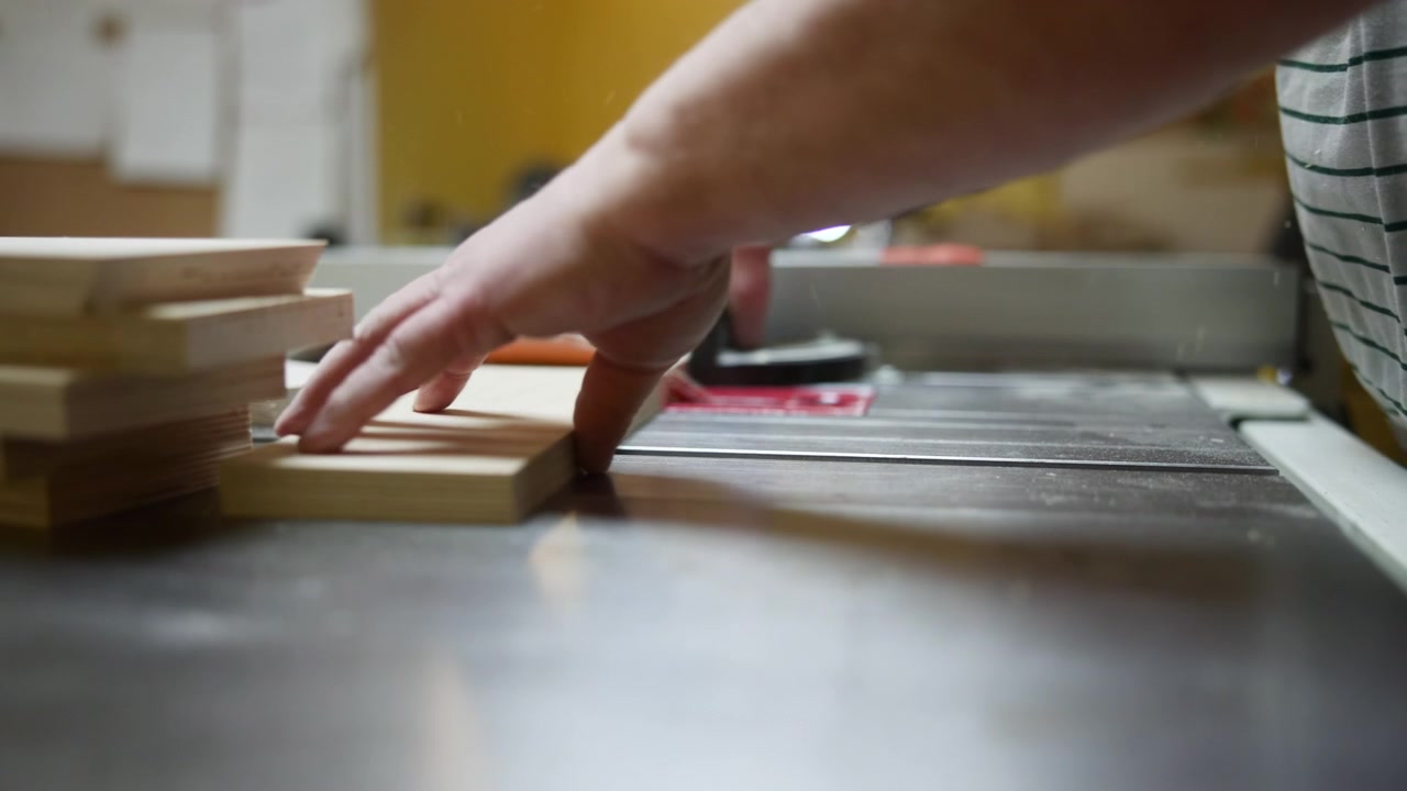 Hands Operating Table Saw Cutting Wood, Closeup Of Craftsman Pushing Small Boards Past Red Blade With Safety. Media