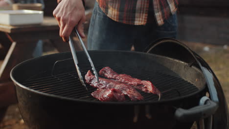 man placing meat steak on grill with tongues