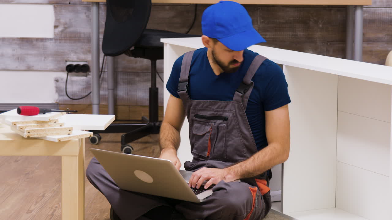 Man with Laptop Assembling Furniture