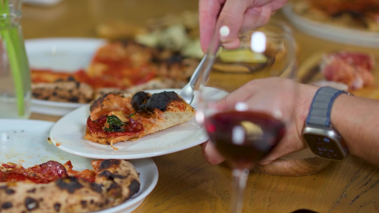 Primo piano di mani che servono fette di pizza sui piatti durante una cena sociale