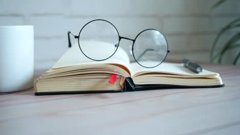 open book with glasses and pen on wooden table