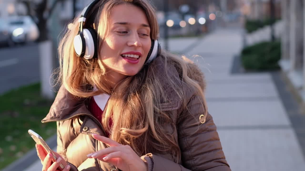 Woman listening to music in her headphones while singing along and dancing in the street