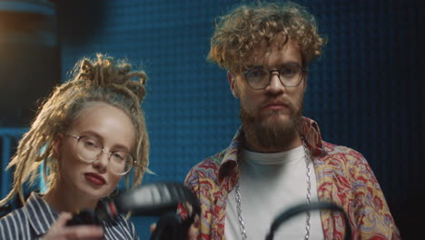 portrait shot of the happy young hipster girl and guy standing at the sound studio with headphones, getting ready to record and smiling to the camera