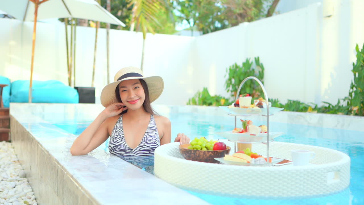 Good looking, happy, Asian woman relaxing in pool with floating breakfast tray
