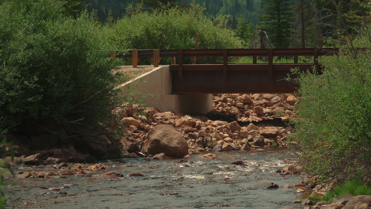 Rushing Water At The Rocky River Under Wooden Bridge. Tilt-up Slow Motion Shot