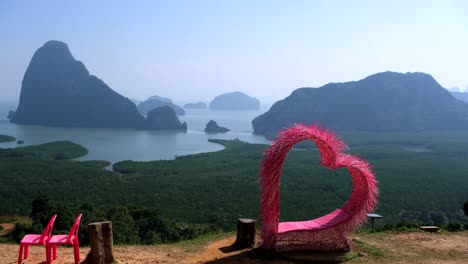 A-stunning-cinematic-vista-in-4K-resolution-features-a-picturesque-scene-comprising-a-serene-lake,-peculiar-rocks-of-varying-sizes,-a-prominent-pink-heart-shape,-and-2-plastic-chairs