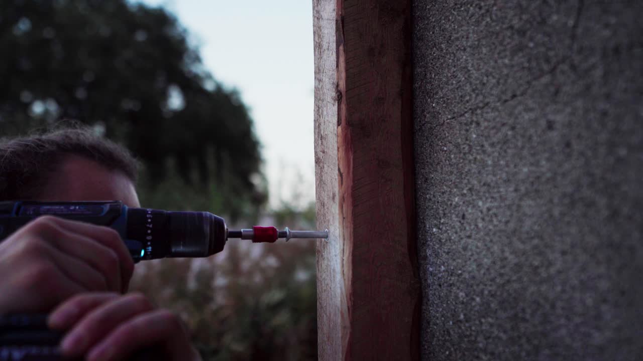 un hombre está clavando un clavo en la madera usando un taladro destinado a la construcción de un invernadero en indre fosen, noruega - de cerca