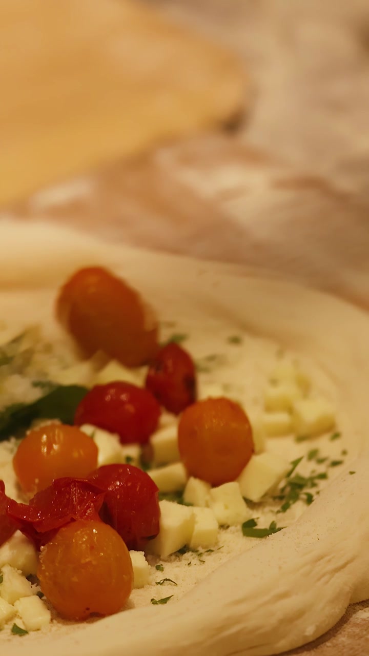 Lenta panoramica della telecamera su impasto crudo per pizza condito con pomodori, formaggio e foglie di basilico fresco.