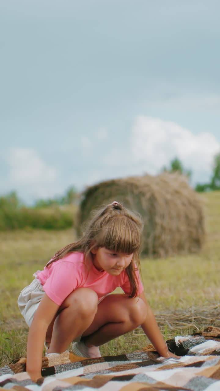 여성과 어린 소녀가 열린 농지에서 체크 된 담요를 펴고 구름이 은 하늘 아래 근처에 서있는 사람들과 함께, 조용한 시골 시골 설정에서 야외 피크닉 준비