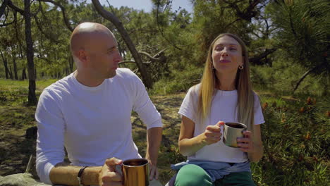 happy couple drinking from mugs in forest