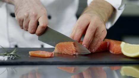 chef cutting salmon fillet at kitchen. closeup hands slicing fresh fish.