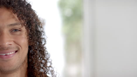 Half-portrait-of-happy-biracial-man-with-long-curly-hair-smiling-at-home,-copy-space,-slow-motion