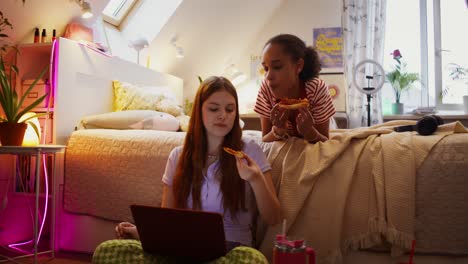 teenage girls enjoying pizza and a laptop in bedroom