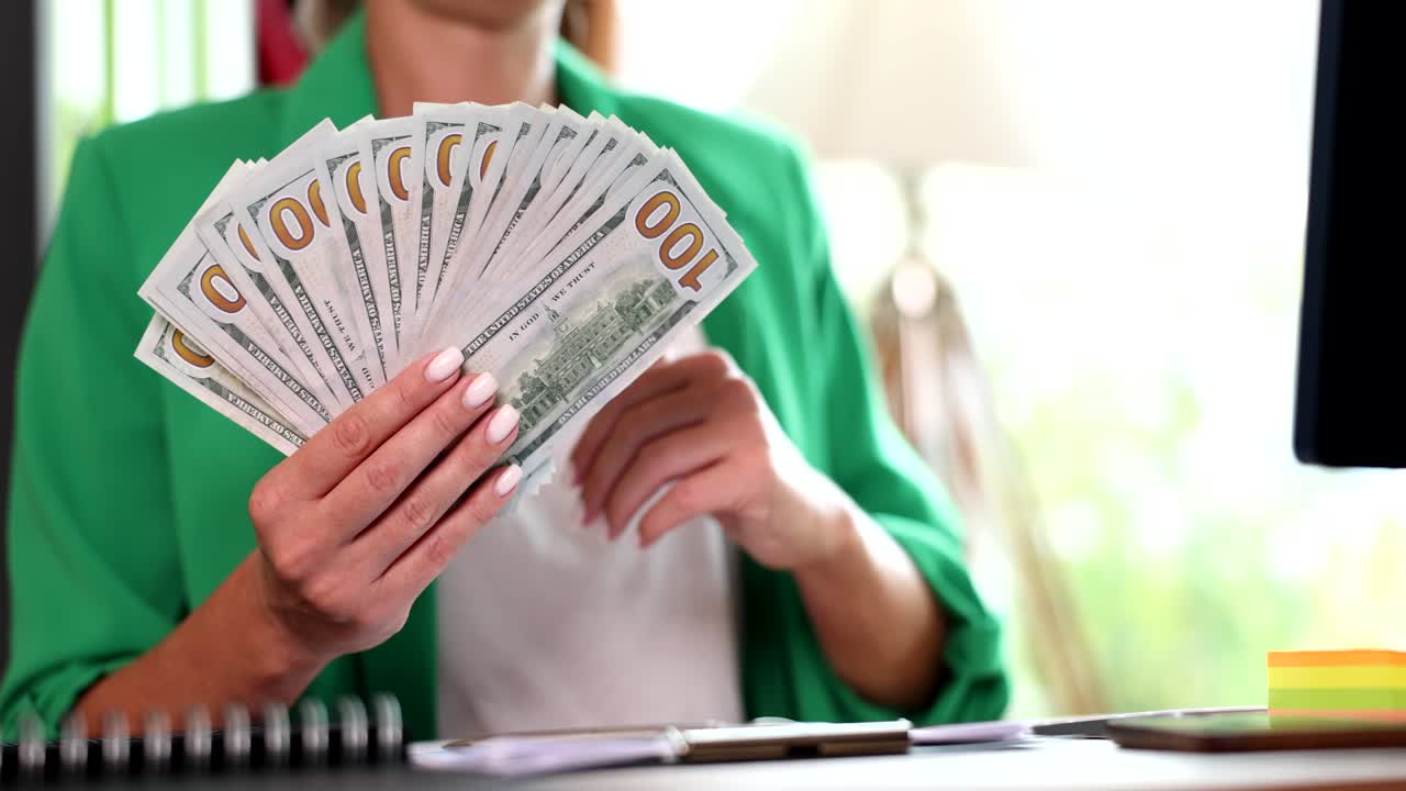 Kvinde holder en stak hundred dollarsedler og giver tommel op