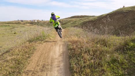 aerial forward dolly shot of a motocross track in malaga spain while a motocross rider drives into the picture and jumps over a hill performing a breathtaking stunt