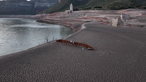 naufragio de un barco en las costas secas de sau marsh con ruinas de la iglesia en el fondo, cataluña, españa