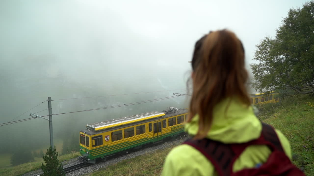 mujer mirando el tren wengernalpbahn pasar lentamente en los alpes suizos