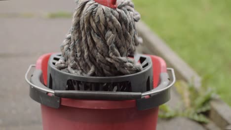 wringing cleaning mop into red bucket wide shot