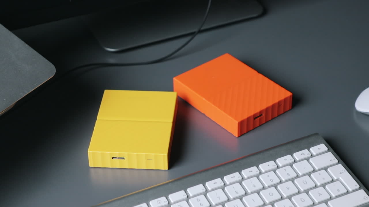 manos masculinas configurando dos discos duros de color amarillo y naranja en una mesa gris en medio del teclado y el mouse