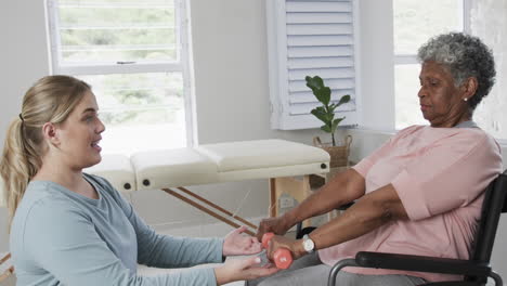 caucasian nurse with senior woman in wheelchair exercising with copy space, slow motion