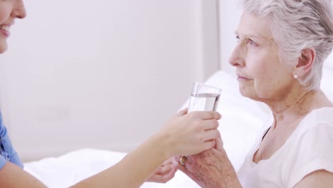 smiling nurse giving water to senior woman in bed