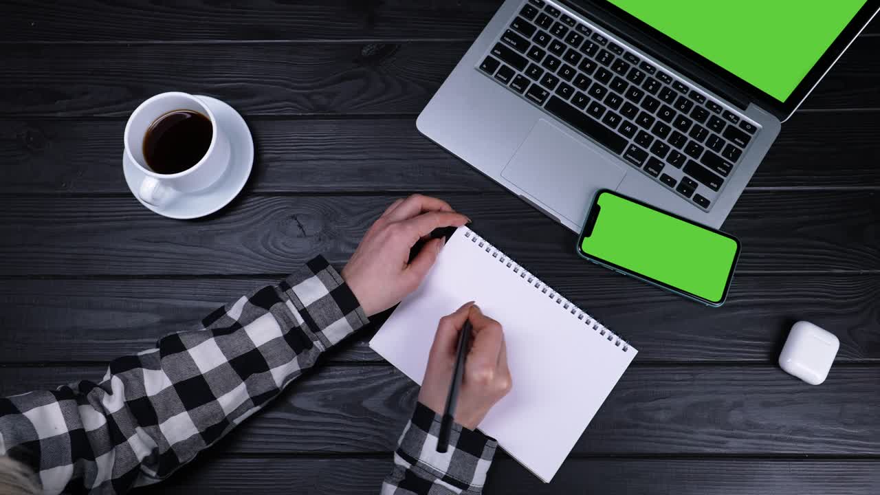 Sale 50 percent, a girl writes a note with a pen in a notebook, top view. A girl sits at a table with a laptop with a green screen and a phone with a chrome key. Slow motion. Close up