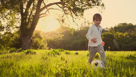 happy boy running with soccer ball running at sunset in summer field.