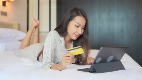 joven asiática en la cama, comprando en línea o revisando una cuenta bancaria con una computadora portátil