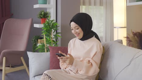 Junge-Arabische-Muslimische-Frau-Im-Hijab-Nutzt-Smartphone-Zu-Hause.