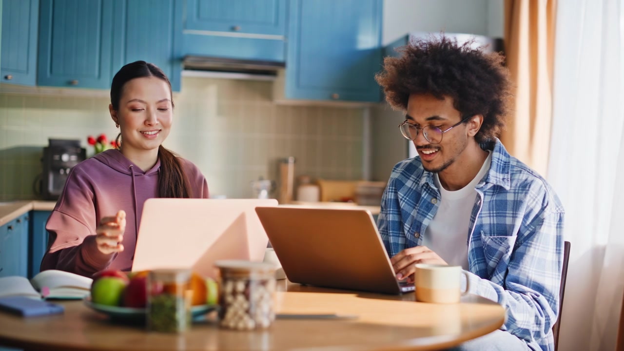 Multiethnic couple working on laptops in kitchen. Asian girlfriend chats