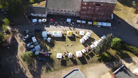 top view of small colorful tents in a farmers market next to a red brick factory building in a warm sunny day