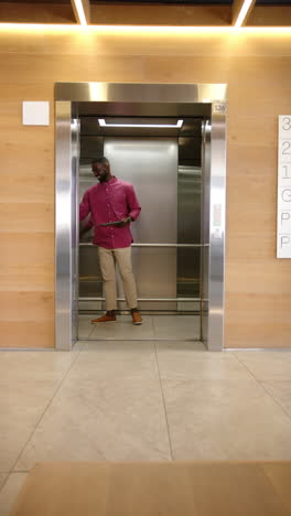 Vertical video: Using tablet, man standing in elevator, multitasking in office building