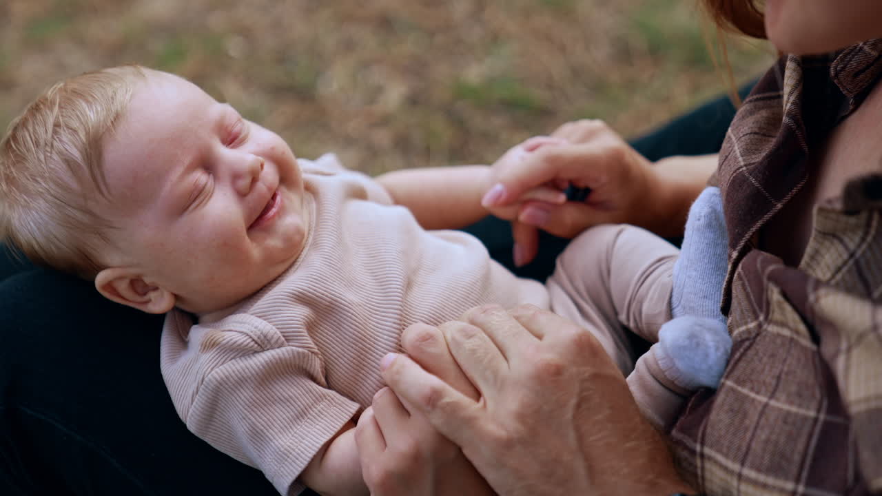 Unrecognized mother holding a baby on her laps. Mom talks to her beloved child and tiny kid smiles in response.