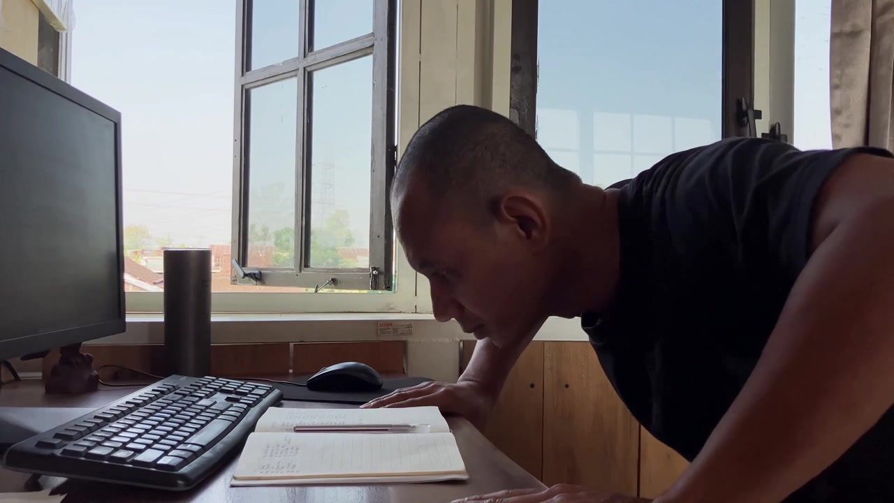 Un uomo con una maglietta nera si prende una pausa dal suo laptop per fare esercizio, eseguendo flessioni inclinate appoggiandosi alla sua scrivania in legno dell'ufficio di casa