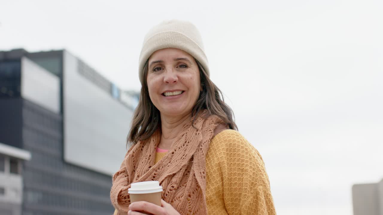 Frau auf dem Dach trägt senfgelben Pullover, hält eine Kaffeetasse und dreht den Kopf neben Bürotürmen.