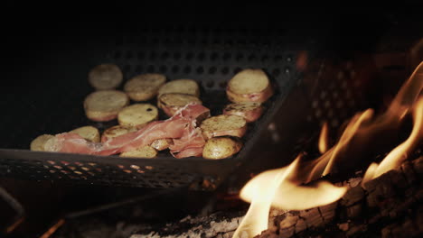 potatoes with pieces of bacon are fried in a frying pan over an open fire