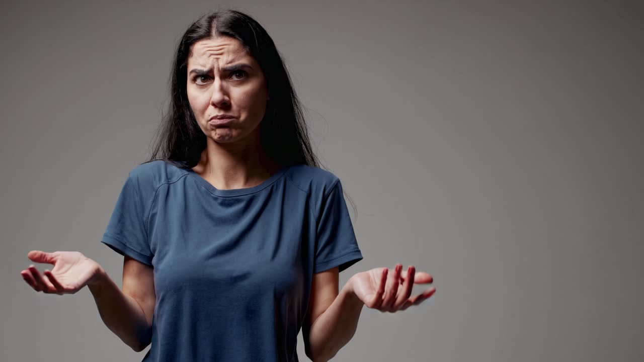 Una mujer se encoge de hombros con expresión de desconcierto, en un plano medio y con un fondo gris.