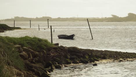 4K-small-wooden-boat-anchored-in-Ria-de-Aveiro,-boat-moving-in-the-wind-and-river-current,-60fps