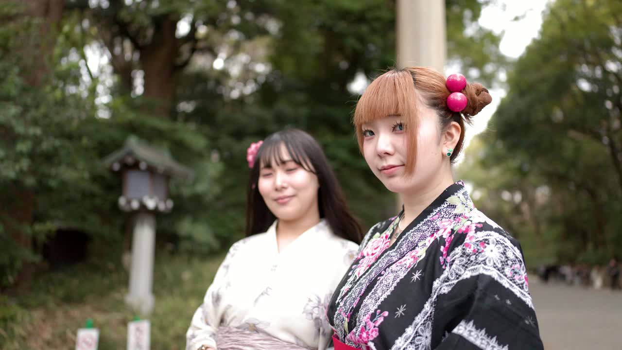 Due donne che indossano kimono tradizionali stanno davanti a un cancello torii di legno al Santuario Meiji.