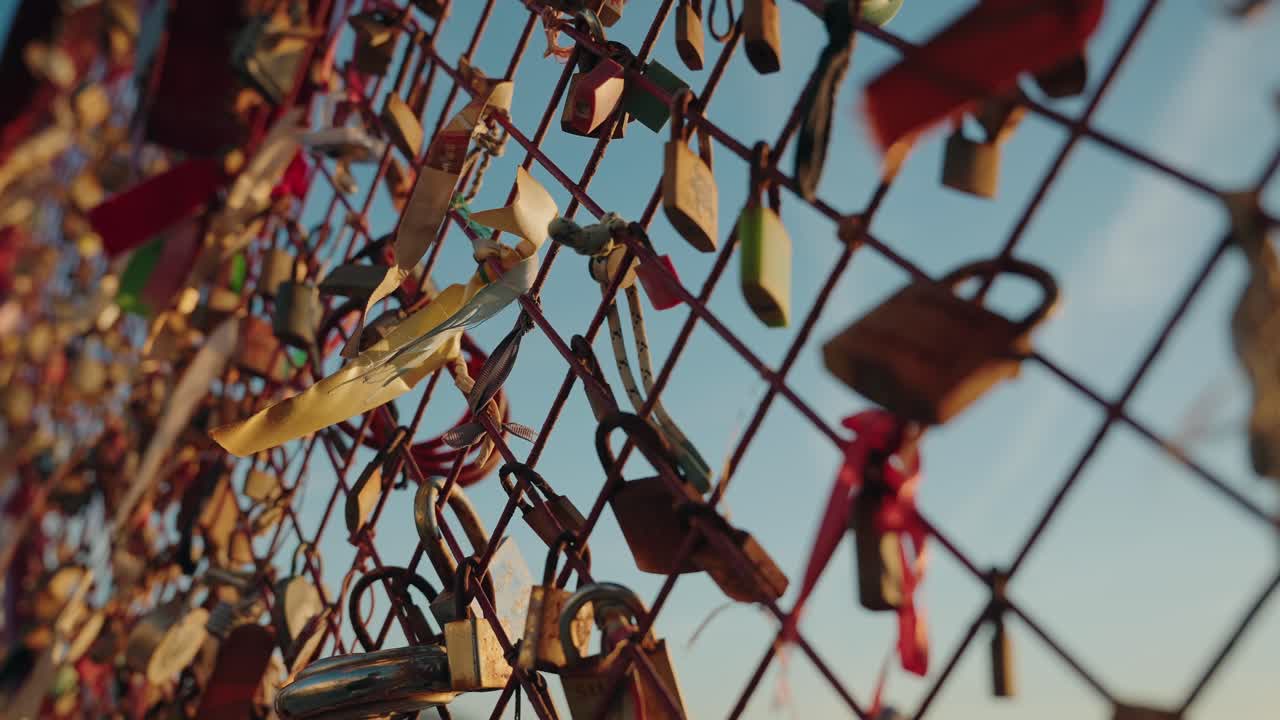 Sunlit love locks and tattered ribbons dance on a metal fence, holding secrets of hearts