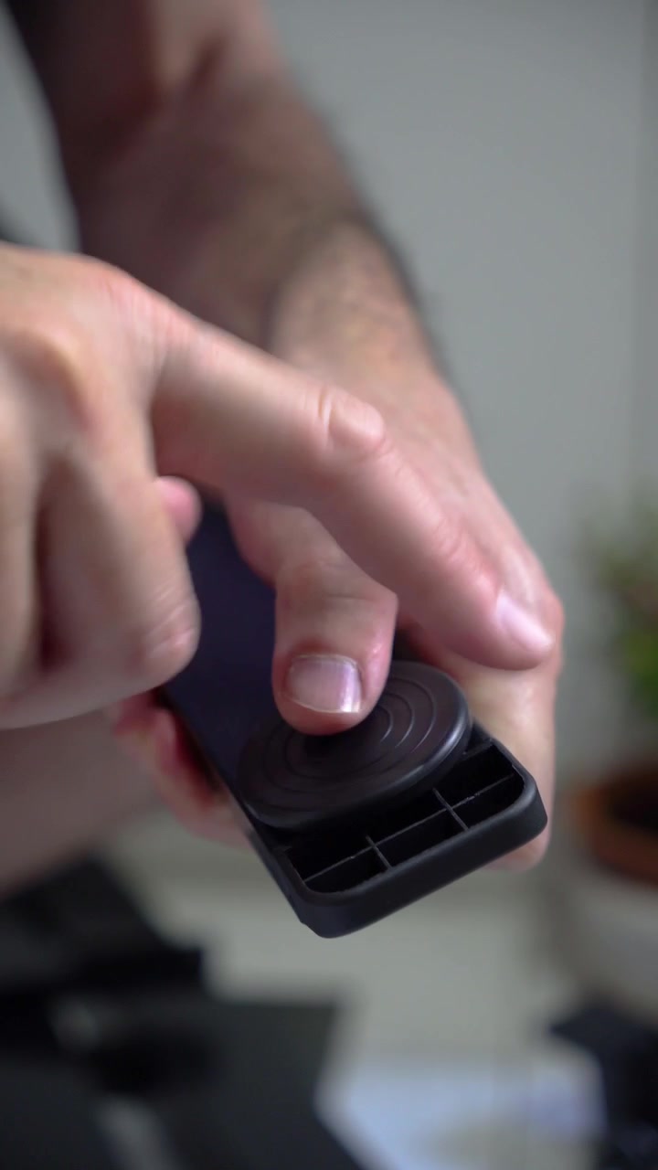 Inquadratura verticale ravvicinata delle mani di un uomo adulto che avvitano e ruotano un piedino livellatore rotondo in plastica nella base di una barra di mobile nera. Progetto fai da te per la casa, azione manuale