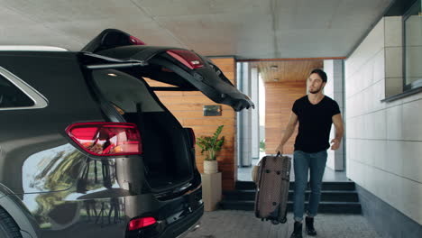 caucasian man loading suitcase in black car in luxury garage.