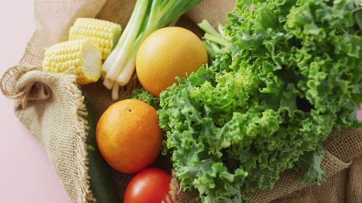 Video of fresh fruit and vegetables in rustic bag over pink background